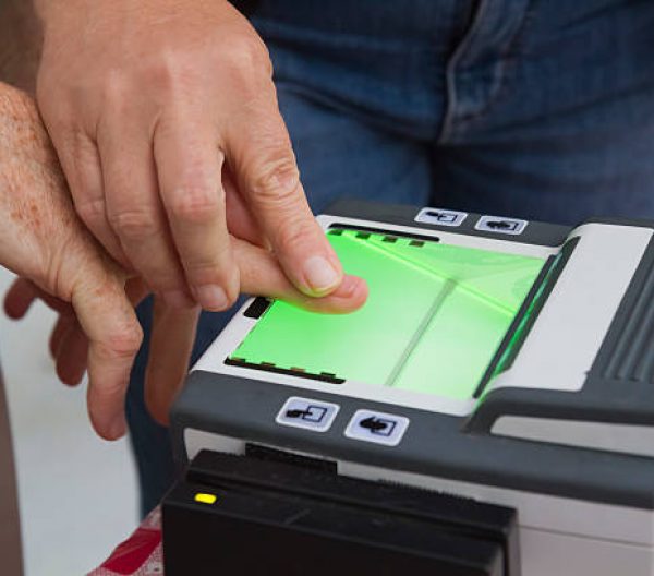 Close-up of a digital fingerprint scanner as an elderly person is being assisted in getting their fingerprint recorded.  Some blur and noise as this was taken at a community senior safety event.